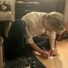 a man sitting on the floor writing in front of a bottle of beer and papers