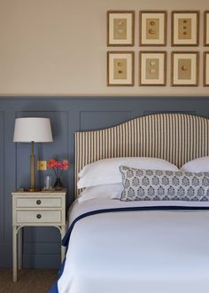 a bed with white sheets and blue pillows in a bedroom next to pictures on the wall