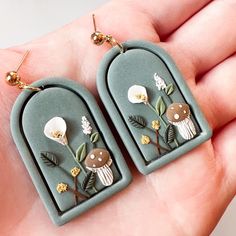 a pair of earrings with flowers and mushrooms on them are being held in someone's hand