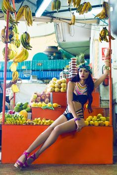 a woman sitting on top of a fruit stand