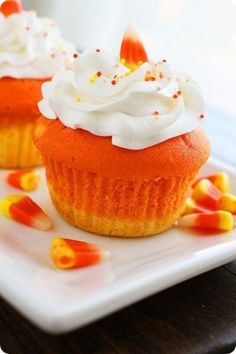 two cupcakes with white frosting and candy corn on a small square plate