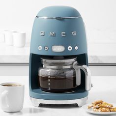 a blue coffee maker sitting on top of a counter next to a plate of food