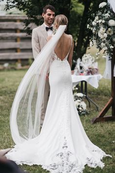 a bride and groom standing under an arch with their veil blowing in the wind as they look at each other