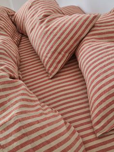 an orange and white striped comforter with pillows on it's sides, in front of a window