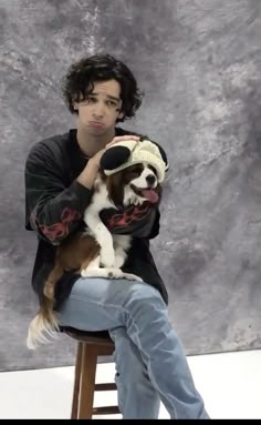 a man sitting on a stool holding a dog wearing a knitted hat and sweater