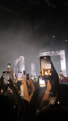 people holding up their cell phones in front of the crowd at a music concert with lights on