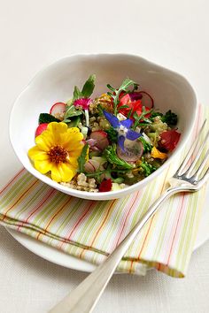 a white bowl filled with vegetables on top of a striped napkin next to a fork