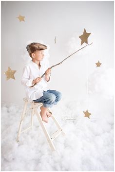 a young boy is sitting on a stool holding a wand in his hand and looking at the stars