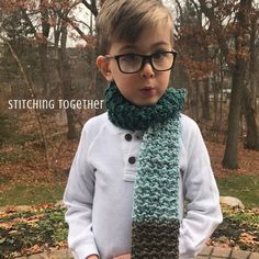 a young boy wearing glasses and a knitted scarf with buttons on the end, standing in front of trees