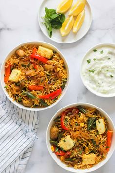 three bowls filled with rice and vegetables next to lemon wedges on a white table