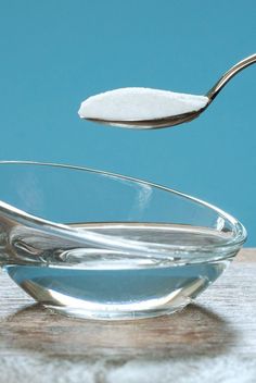 a spoon with some sugar in it on top of a glass bowl filled with water