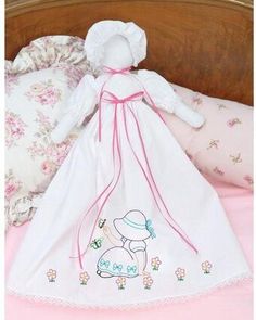 a doll is laying on the bed next to some pillows and blankets with pink trimmings