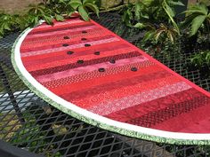 a red and white surfboard sitting on top of a black table next to trees