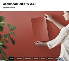 a woman holding a piece of paper in front of a red wall with the words cochheal red v - 3 30 on it