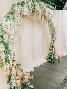 a wedding arch decorated with white flowers and greenery, lit by candles on the floor