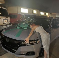 a woman leaning on the hood of a car with a green ribbon tied around it