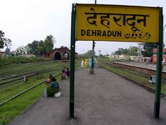 people sitting on the ground in front of a train station sign that reads dehradin