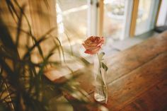 a single rose in a vase sitting on a wooden table next to a glass door