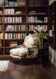 a chair in front of a book shelf filled with lots of books and vases