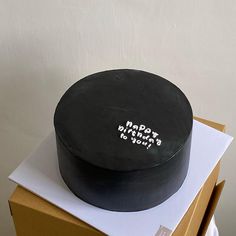 a black cake sitting on top of a cardboard box with writing on the inside of it