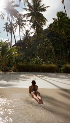 a woman laying on her stomach in the water near some palm trees and beach grass