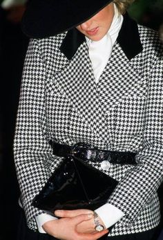 a woman in a black and white coat is holding a handbag while wearing a hat