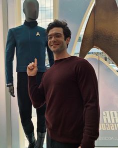 a man standing in front of a star trek uniform and giving the peace sign with his hand