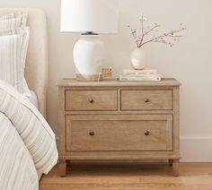 a white vase sitting on top of a wooden dresser next to a lamp and bed