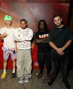 four young men standing next to each other in front of a red and orange wall