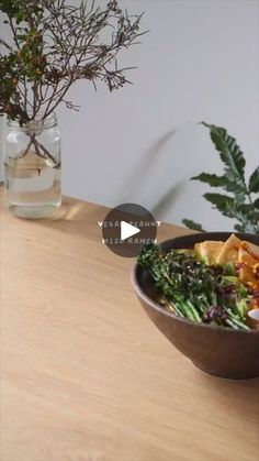 a wooden table topped with a brown bowl filled with food next to a vase full of plants