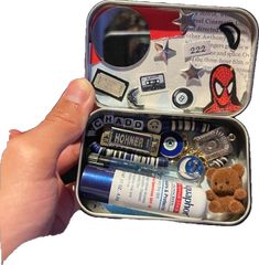 someone is holding an open tin with various items in it, including a teddy bear