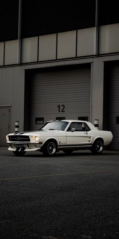 a white muscle car parked in front of a garage