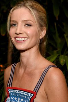 a woman with blonde hair and blue eyes smiles at the camera while standing in front of some plants