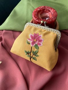 a small purse with a flower on it sitting on a pink blanket next to a candle