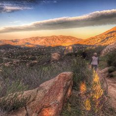 a person walking up a dirt path in the mountains at sunset or sunrise with clouds overhead