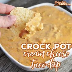 a hand holding a cracker over a bowl of cream cheese taco dip