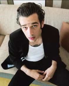 a man sitting on top of a couch wearing a black blazer and white t - shirt