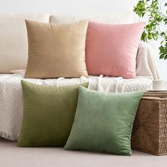 four different colored pillows sitting on a couch next to a wicker basket and potted plant