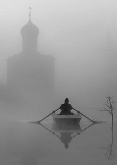 a person in a row boat on a body of water with a church steeple in the background