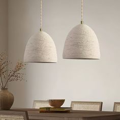 two lamps hanging over a dining room table with chairs and a bowl on the table