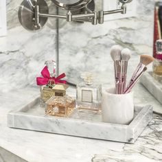 a marble tray with makeup brushes and perfume bottles