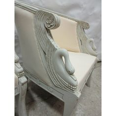 a white chair with an intricately carved arm and back, sitting on a carpeted floor