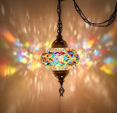 a multicolored lamp hanging from a chain in front of a wall with light coming through it