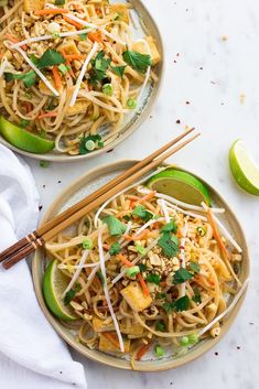 two plates filled with noodles, carrots and cilantro on top of a white table