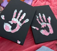 two handprints on black canvases with pink and white paint are sitting next to each other