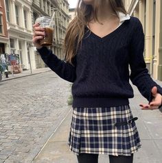 a girl in a plaid skirt is holding a drink