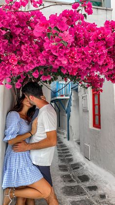 a man and woman kissing under a tree with pink flowers hanging over the top of their heads