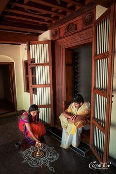 two people sitting on the floor in front of an open door and looking at something