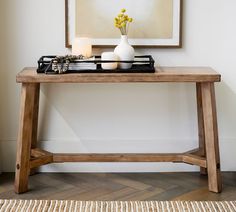 a wooden table topped with a white vase filled with yellow flowers next to a painting