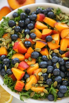 a white bowl filled with blueberries, peaches and kale on top of a table